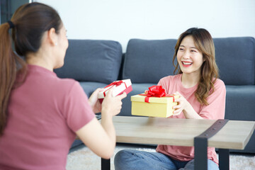 young woman giving gift box to her friend for birthday on a table