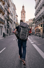 young caucasian man running along the asphalt of a city street with a backpack on his back barefoot with dirty feet, valencia, spain