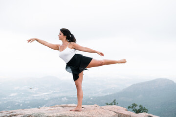 Caucasian brunette mature woman with long hair smiling doing ballet movements on the big rock in...