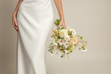 Unrecognizable cropped woman in white elegant silk dress with white bouquet of natural flowers in...