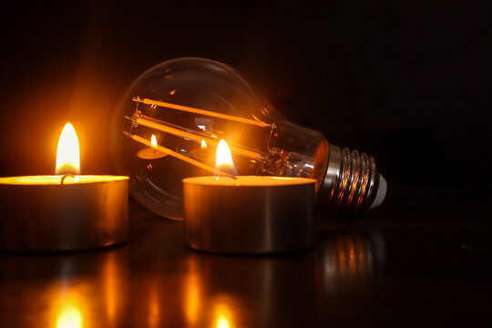 Lightbulb With Candles In The Background. Concept Of Loadshedding, Power Cuts Or Blackouts. Loadshedding In South Africa, Power Utility Enforced Reduction In Electricity Usage To Protect The Grid