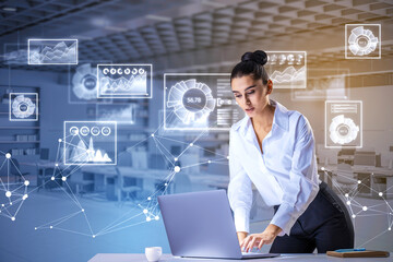 Obraz premium young european businesswoman using laptop while standing at desk in toned office interior with glowing business charts. Statistics, Growth and Analysis Information concept. Double exposure.