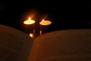 book and candle. Lightbulb with candles in the background. Concept of loadshedding, power cuts or...