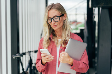 Elegant blond business woman in pink jacket holding laptop computer