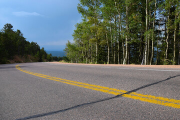Empty, abandoned road with bright yellow marking strip in the Colorado mountains with aspen trees