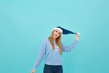 young woman in a New Year's hat on a blue background. woman hold a New Year's hat in her hands. Christmas or new year celebration on blue background