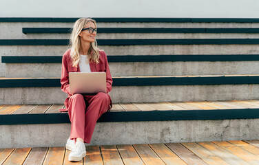 Modern business woman sits and on an urban design and works on a laptop.