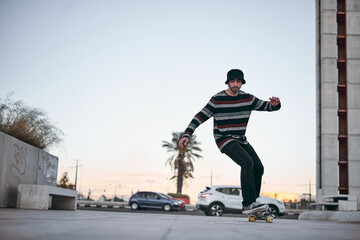 caucasian boy in striped sweater with nose piercing and cute beanie having fun on a skateboard in...