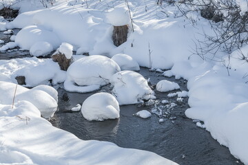 Flowing river water among snowdrifts in winter