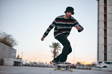 caucasian guy in striped sweater with nose piercing and nice beanie concentrated on a skateboard in...