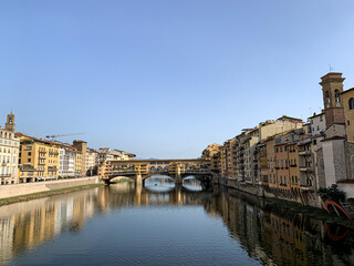 Fototapeta na wymiar Firenze, Tuscany, Italy - 18.10.2022. Ponte Vecchio Bridge during beautiful sunny day with reflection in Arno River, Florence, Italy. Picturesque medieval arched river bridge with Roman origins, lined