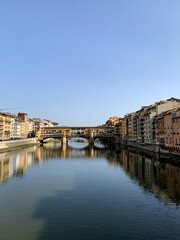 Firenze, Tuscany, Italy. Ponte Vecchio Bridge during beautiful sunny day with reflection in Arno River, Florence, Italy. Picturesque medieval arched river bridge with Roman origins, lined