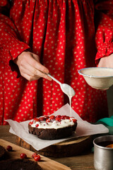 A woman prepares a Christmas chocolate cake with cherries, close-up