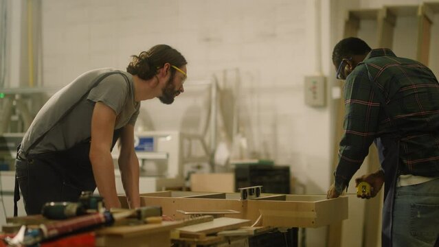 young hipster carpenter man carpenter and black colleague Using Tape Measure and making woodworks handcrafted furniture in wood workshop.carpenter at work measuring wooden planks by Cartridges Meters