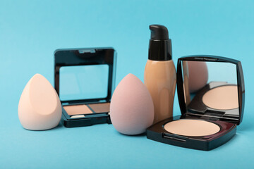 Beauty blender, foundation, concealer, blush,powder and makeup brushes composition on blue...