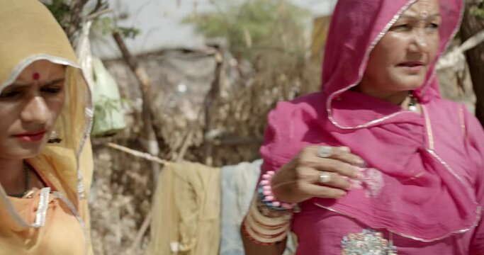 Horizontal footage of two women of the nomadic tribe wearing yellow and pink saris talking