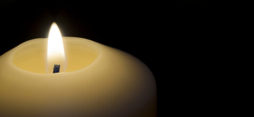 lit candle in the foreground with black background. Candlelight