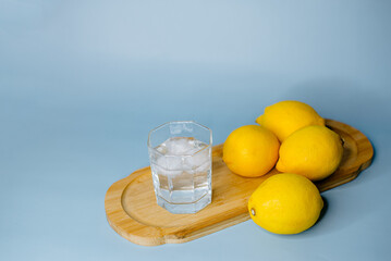 yellow lemons lie on a wooden board with a glass of water on a blue background