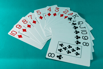 A fan of white cards of diamonds and cross suits, red and black, respectively, on a turquoise background.