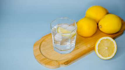 yellow lemons lie on a wooden board with a glass of water on a blue background