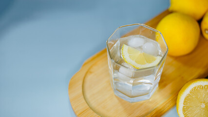 yellow lemons lie on a wooden board with a glass of water on a blue background