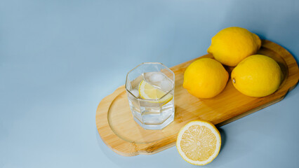 yellow lemons lie on a wooden board with a glass of water on a blue background