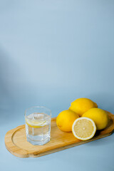 yellow lemons lie on a wooden board with a glass of water on a blue background
