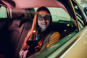Business woman using smartphone while sitting in a backseat of a car at night