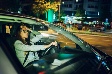 Tired business woman driving a car in a city during a night