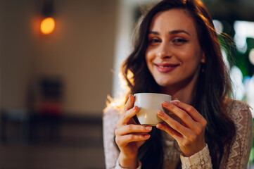 Portrait of beautiful young woman drinking coffee or tea in a cafe