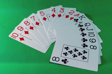 A fan of white cards of diamonds and cross suits, red and black, respectively, on a green background.
