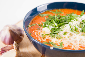 Italian tomato soup served with cream, mozzarella cheese and fresh parsley in a bowl, on a wooden  pad decorated with garlic
