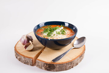 Italian tomato soup served with cream, mozzarella cheese and fresh parsley in a bowl, on a wooden  pad decorated with garlic