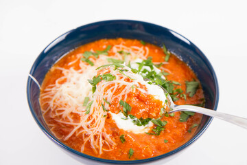 Italian tomato soup served with cream, mozzarella cheese and fresh parsley in a bowl, eaten with a spoon