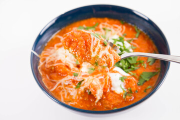 Italian tomato soup served with cream, mozzarella cheese and fresh parsley in a bowl, eaten with a spoon