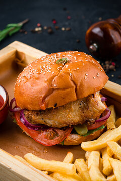 American chicken burger with tomato, pickle, onion, lettuce, cheese sauce on a wooden board with french fries and ketchup.