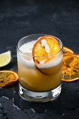 Alcoholic cocktail Whiskey Sour from whiskey, egg white, lemon juice, syrup and lime garnished with an orange slice.
