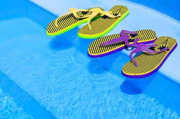 Bright and colorful flip-flops with starfish on the background of the pool.