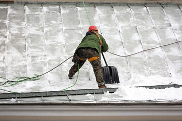 Woman worker removing snow on the roof of a building. Snow removal, climber cleaning roof in winter