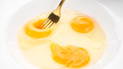 Stirring eggs with fork in white plate, close up. Cooking French omelette