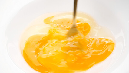 Stirring eggs with fork in white plate, close up