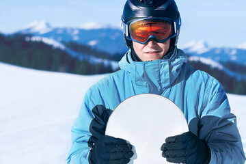 Portrait of man at the ski resort on the background of mountains and blue sky,  hold snowboard....