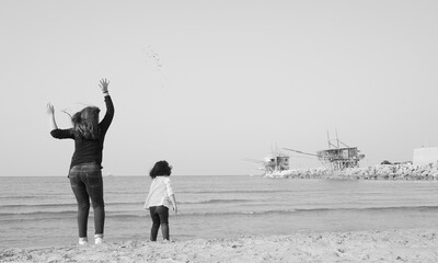 Foto di due bambine che giocano sulla spiaggia. Una bambina salta lanciando delle pietre, l'altra...