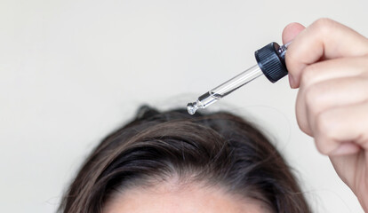 woman applying serum oil on wet hair with pipette or using white comb to disentangle...