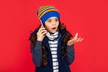 shocked teen girl in down vest with smartphone. portrait of child greeting while phone conversation.