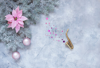 Miniature golden saxophone copy, snowy fir tree branches, gentle poinsettia flower and Christmas pink balls. Christmas and New Year's concept. Top view, close-up