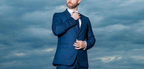 Guy in suit crop view. Unshaven guy adjusting tie outdoors. Professional guy sky background