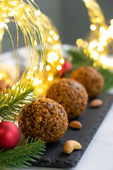Nut cookie balls on black slate board with almond and cashew, Christmas lights and decor on background. Vegan gluten free dessert. Recipe of biscuits for New Year and Christmas holidays menu.