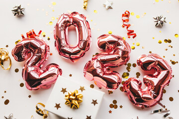 Pink balloons made of foil in the form of numbers 2023 with confetti and a white gift box on a pink...