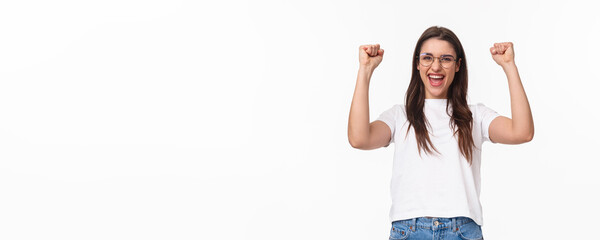 Fototapeta na wymiar Waist-up portrait of talented attractive girl winning in competition, fist pump raising hands up, do champion dance, saying yes achieve success, triumphing over victory, stand white background